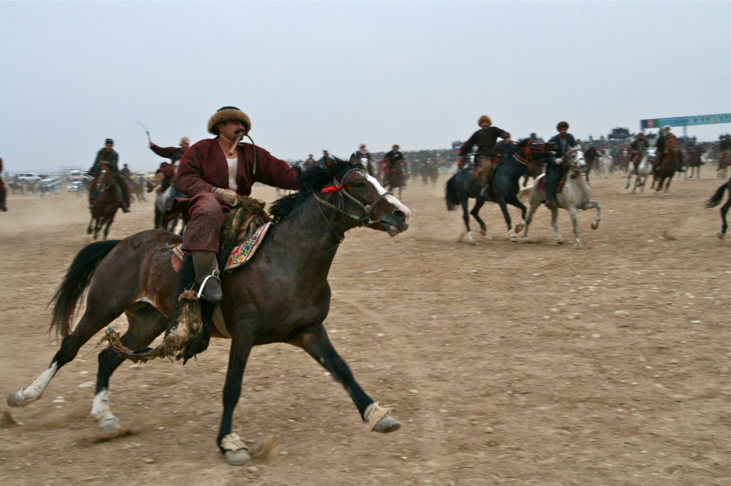 An Afghan Buzkashi player with the Buz (carcass) riding toward the flag at this end of the Buzkashi field.  Mazar-i-Sharif, Afghanistan 2007