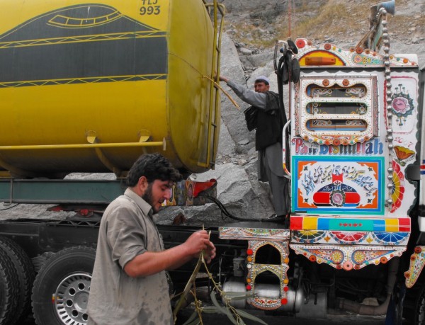 Tghe truck drivers start some damage control efforts by sticking small tree branches into the bullet holes. There are coverd in fuel but doing a good job at protecting the shipment they are responsible for.